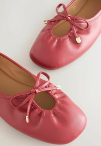 Balerini roșii din piele cu vârf rotund, detaliu cu fundă laterală și decupaj tip cheie. Textură netedă și accente din metal auriu.