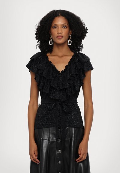 Blusa negra con cuello fruncido y mangas cortas, tejido texturizado, cintura ceñida con un lazo, combinada con una falda de cuero negra.