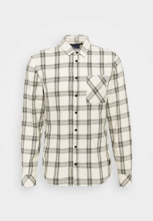 Camisa blanca de manga larga con botones, con patrón de cuadros negros y un bolsillo en el pecho que presenta un diseño de cuadros diagonales.