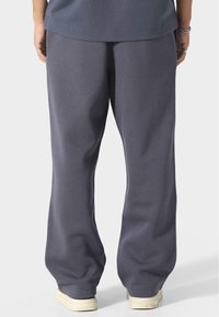 Grå sweatpants med en afslappet pasform, lavet af blødt stof, med elastisk talje, sidelommer og ribkant forneden. Bæret med hvide sneakers.