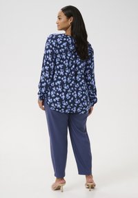 Blusa de manga larga floral en azul marino con flores azules, combinada con pantalones sueltos azul marino, que cuentan con un corte relajado y una textura suave, complementada con tacones beige.