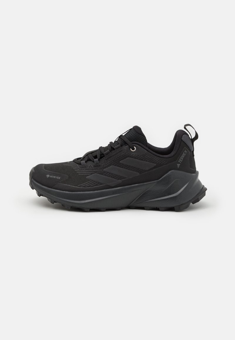 Shoe de trail running preto com um upper texturizado, sistema de atacadores integrado e uma sola robusta com padrões de tração proeminentes.