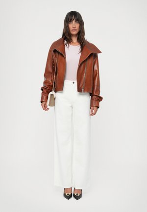 Brown leather cropped jacket with wide collar, light pink top, white wide-leg trousers, and black pointed shoes with gold accents.