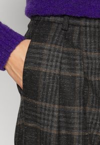 Pantaloni gri în carouri, realizati dintr-un material texturat cu un model de carouri maro, având buzunare laterale și o croială ajustată la talie.