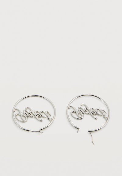 Ασημένια κρίκοι σκουλαρίκια με τη λέξη "ευχαριστημένος" γραμμένη μέσα σε κάθε κρίκο, που βρίσκονται πάνω σε λευκή επιφάνεια.