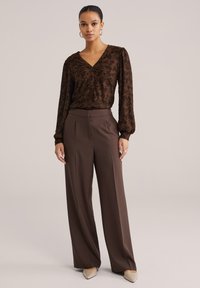 Pruun lillemustriga pluus nööpide ja puffy varrukatega, kombineeritud kõrge vöökohaga, laiade jalgadega pruuni pükstega ning teravate beežide kingadega.