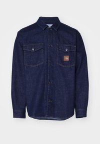 Dark blue denim shirt with long sleeves, button-up front, two chest pockets, and a leather logo patch on the left pocket.