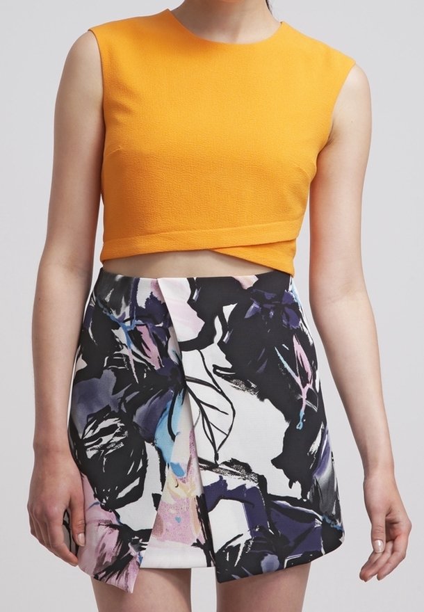 Femme portant un crop top orange sans manches et une mini-jupe taille haute à motif floral abstrait avec détail en couches.
