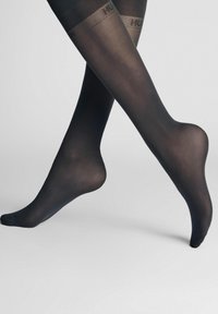 Schwarze, transparente Strumpfhosen mit einem strukturierten oberen Bündchen. Das Material ist glatt mit einem leichten Glanz und betont elegant die Form des Beins.