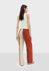 Pantaloni a gamba larga a righe multicolori con tonalità di rosso, beige e marrone. Realizzati in un tessuto testurizzato con vita alta e tasche laterali.