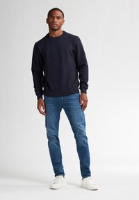 Felpa in cotone navy con collo a giro e polsini a coste, abbinata a jeans in denim azzurro e sneakers bianche. Design semplice e casual.