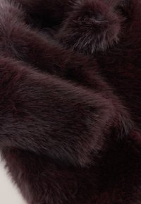 Fourrure synthétique bordeaux avec une texture dense et douce, présentant des longueurs de fibres variées et un détail de pompon duveteux.