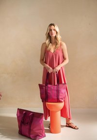 Pink and purple striped tote bags with dual handles; smooth material; one bag on an orange pedestal, another on the floor. Simple design.