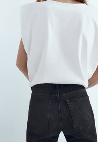 Chemise en coton blanc avec des épaulettes, assortie à un jean noir en denim avec un design classique à cinq poches et des détails de couture subtils.