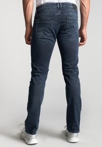 Jeans en denim bleu foncé avec une coupe slim, dotés de poches arrière et d'un accent de taille noir. Texture lisse avec un léger délavage.