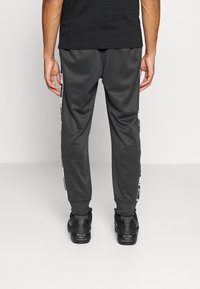 Grå träningbyxor med en slät textur, med vita sidostråk och elastiska mudd, kombinerat med svarta träningsskor.