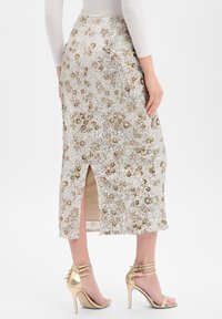Midi-Rock aus Pailletten in Silber mit goldfarbenen Blumenverzierungen, mit einem Schlitz hinten und einem glatten Innenfutter. Kombiniert mit goldenen Absätzen.