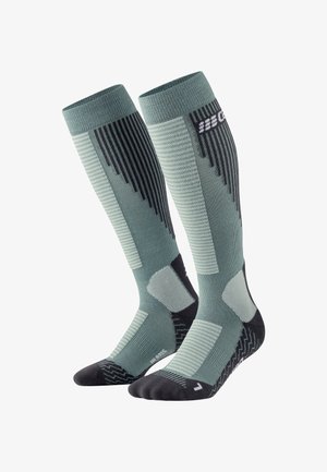 Calze compressive verdi e nere, con texture a coste e con motivo, tallone e punta rinforzati, con dettaglio del logo vicino alla parte superiore.