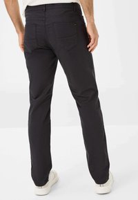 Zwarte katoenen broek met een recht model, voorzien van twee achterzakken en een tailleband. Draagt met witte sneakers.