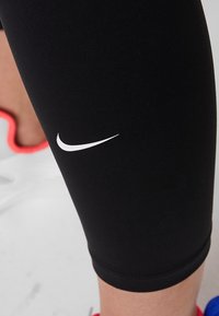 Czarne legginsy sportowe wykonane z elastycznego materiału, z białym logo Nike na udzie i dopasowanym krojem.