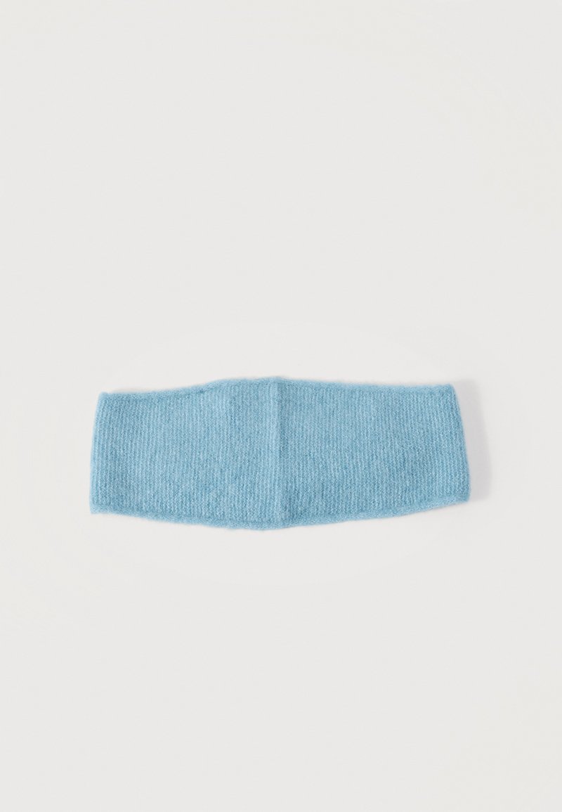 Bandeau tricoté bleu clair et doux avec une couture au centre, posé à plat sur un fond blanc.