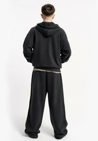 Czarna, oversize bluza z szerokimi rękawami, w połączeniu z luźnymi czarnymi spodniami. Miękka tekstura tkaniny, minimalistyczny design, brak widocznych wzorów.