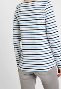 Maglia a maniche lunghe bianca con strisce verticali blu navy e azzurro chiaro, presenta un collo rotondo e un piccolo logo sul retro.