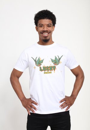 Hvid bomulds t-shirt med grønne og gule svaleillustrationer, med ordene "LUCKY sailor" i orange, placeret på en lys baggrund.