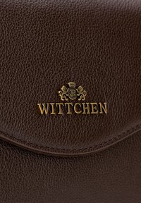 Hnědá kožená kabelka s texturovaným povrchem, která má zlaté logo "WITTCHEN" a zakřivený klopový vršek s detailem prošívání.