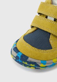 Baskets en daim jaune avec mesh bleu marine, brides velcro, et semelle en caoutchouc à motifs multicolores avec des accents bleus et jaunes.