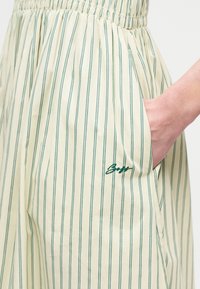 Jupe à rayures verticales vertes avec bande élastique à la taille, avec une main dans la poche latérale et un petit logo brodé près de la poche.