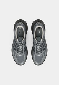 Par tenisica za trčanje Adidas Adizero u sivoj boji s mrežastim gornjim dijelom i crnim potplatima, prikazano iz ptičje perspektive na bijeloj pozadini.