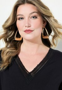 Zwarte kleding met een V-hals en ingewikkelde kantdetails. Grote gouden oorbellen accentueren de look, aangevuld met zacht golvend haar.