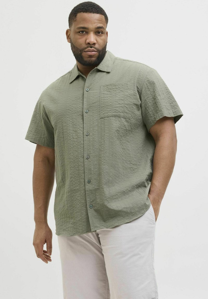 Košulja kratkih rukava, s dugim kopčanjem u svijetloj maslinastoj boji, s teksturiranim materijalom, s džepom na prsima i ovratnikom.