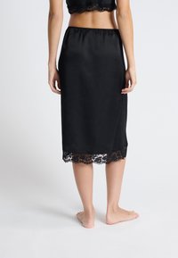 Czarna satynowa spódnica w kształcie slip z elastycznym pasem, ozdobiona koronkowym wykończeniem na dolnej krawędzi. Gładka faktura, średnia długość.