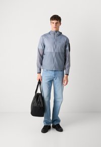 Light blue windbreaker jacket with a hood, contrasting gray sleeves, and a zip front; paired with light denim jeans and a black bag.