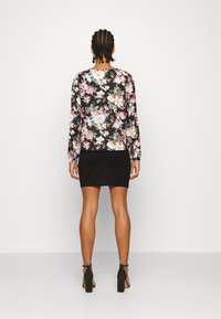 Blommig långärmad topp med svart bas, prydd med rosa och vita blommor; kombinerad med en figurnära svart kjol och svarta klacksandaler.
