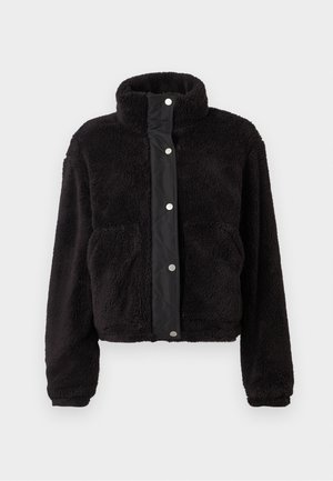 Chaqueta de forro polar negro y esponjoso con cuello alzado, cierre frontal de botones a presión, mangas largas y dos bolsillos laterales sobre un fondo claro.