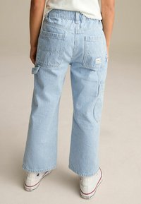 Pantalons larges en denim à rayures bleues et blanches, dotés de poches latérales et arrière, avec un étiquette carrée 'LOVE' au-dessus de la poche droite.