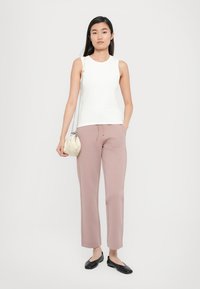 White sleeveless top, light pink tapered pants, black flats, and a small cream handbag, all set against a plain white background.
