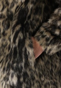 Rjava in črna umetna krznena tkanina z leopardjim vzorcem, ki se ponaša s prijetno teksturo in roko, vidno v stranskem žepu.