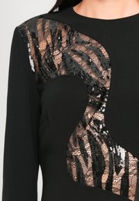 Zwarte jurk met een pailletten dierenprintpaneel op de schouder, gecombineerd met gladde stof; getailleerde vorm met een ronde halslijn.