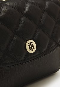 Sort quiltet læderhåndtaske med afrundet klap, guldfarvet logo hardware og en struktureret finish med synlige syningsdetaljer.