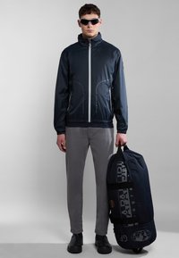 Giacca a vento navy con zip, polsini elasticizzati e due tasche frontali. Pantaloni grigi e un borsone abbinato con stampa del logo.