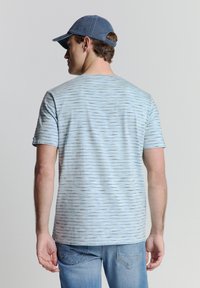Lichtblauw T-shirt met korte mouwen heeft een horizontaal patroon, een zachte textuur en een ronde hals. Gecombineerd met lichtblauwe denim jeans en een blauwe pet.