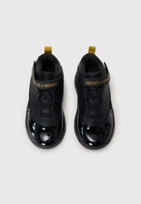 Czarne buty sportowe z błyszczącego lakierowanego materiału, z siateczkową cholewką i żółtą pętelką. Posiadają bezpieczny system sznurowania oraz logo marki.