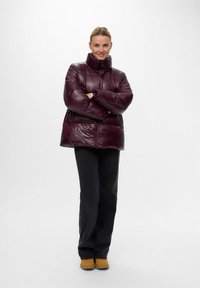Bordeauxfärgad puffjacka med hög krage, som har en glansig yta och horisontell sömnad. Matchad med svarta byxor och gula stövlar.