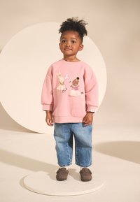 Felpa rosa con illustrazioni di animali, vestibilità ampia, polsini a coste, abbinata a jeans larghi azzurri chiari e scarpe marroni slip-on.