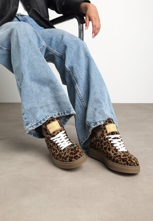 Sneakers con stampa leopardata, finitura testurizzata simile a pelliccia, lacci bianchi e suole color beige. Abbinati a jeans larghi azzurri.