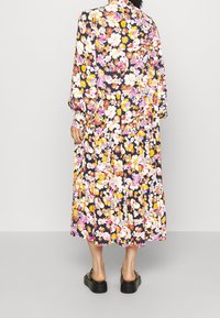 Robe midi fleurie avec un fond sombre et des fleurs éclatantes de rose, jaune et blanc, manches longues et jupe plissée. Chaussures à plateforme noires.